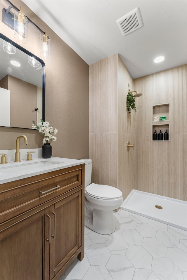 bathroom with tiled shower, tile patterned floors, vanity, and toilet