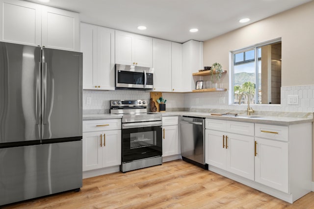 kitchen featuring white cabinetry, sink, backsplash, appliances with stainless steel finishes, and light wood-type flooring