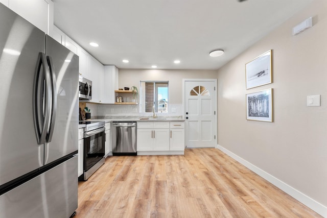 kitchen featuring appliances with stainless steel finishes, light wood-type flooring, tasteful backsplash, sink, and white cabinets