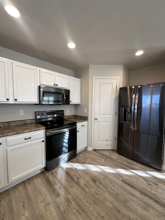 kitchen with stainless steel appliances, white cabinetry, and light hardwood / wood-style flooring