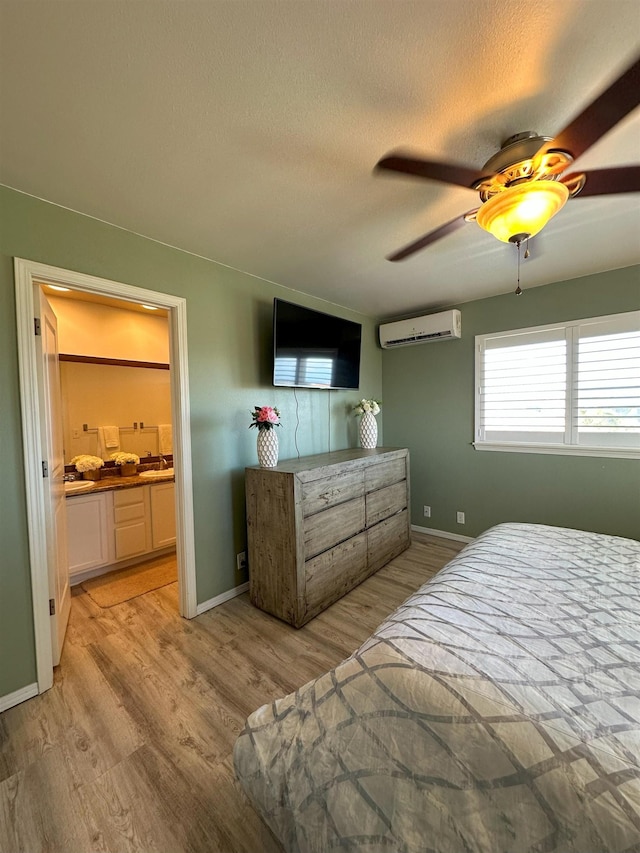 bedroom with ceiling fan, light hardwood / wood-style flooring, ensuite bathroom, and a wall mounted air conditioner