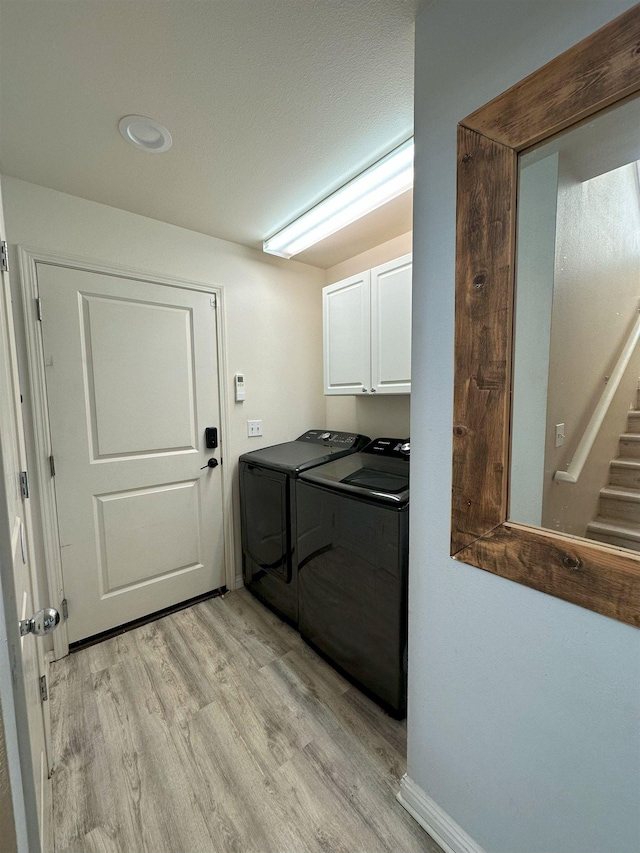 washroom with washing machine and clothes dryer, cabinets, and light wood-type flooring