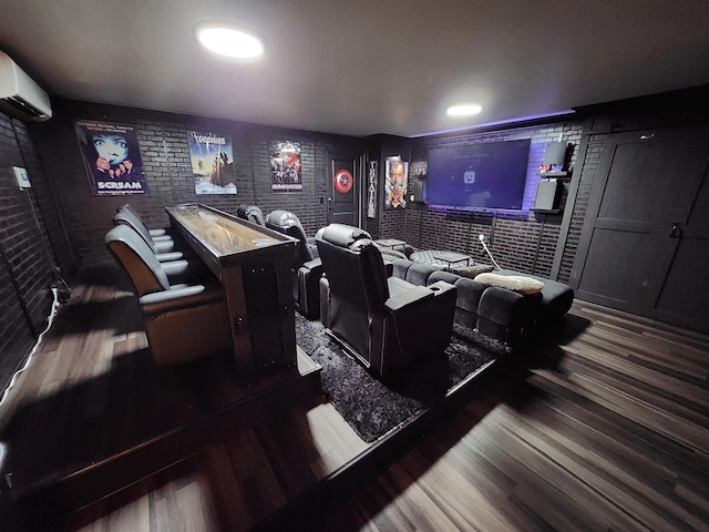 cinema room with a wall mounted air conditioner, dark wood-type flooring, and brick wall