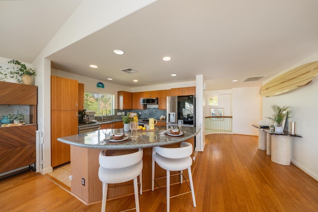 kitchen featuring appliances with stainless steel finishes, a center island, sink, light hardwood / wood-style flooring, and a breakfast bar area