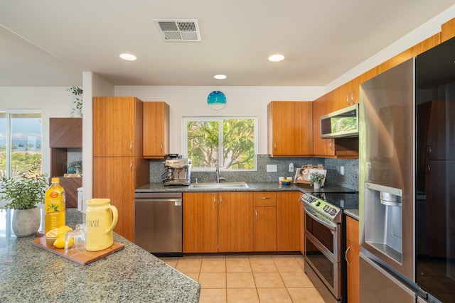 kitchen featuring appliances with stainless steel finishes, sink, light tile patterned floors, stone counters, and decorative backsplash