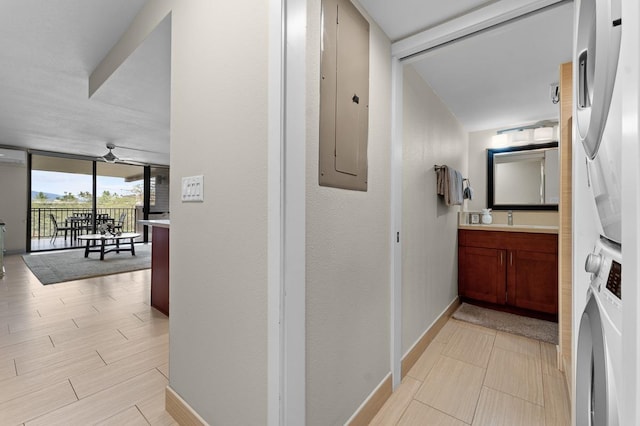 corridor with a wall of windows, stacked washer and clothes dryer, electric panel, and light hardwood / wood-style floors