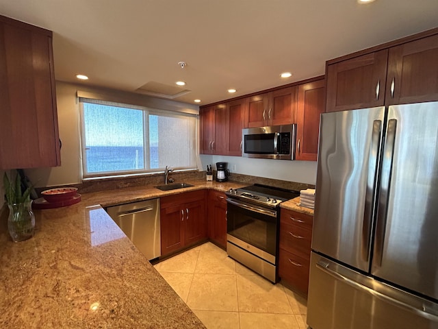 kitchen with light tile patterned floors, light stone countertops, sink, stainless steel appliances, and a water view