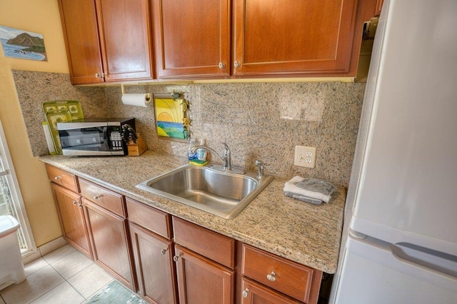 kitchen with decorative backsplash, white refrigerator, light stone countertops, light tile patterned floors, and sink