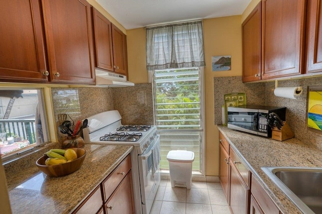 kitchen with decorative backsplash, light tile patterned floors, white gas range oven, and light stone counters