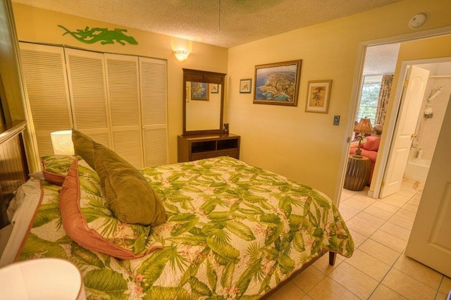 bedroom featuring a closet, ensuite bath, a textured ceiling, and light tile patterned floors