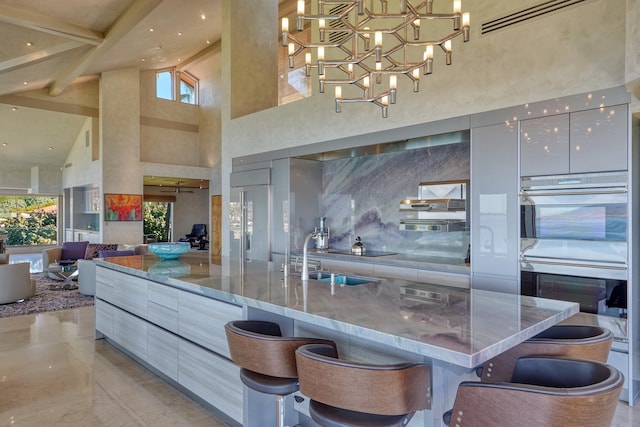 kitchen with high vaulted ceiling, a kitchen bar, stone counters, decorative light fixtures, and a notable chandelier