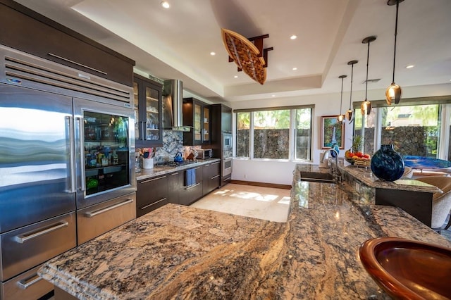 kitchen with appliances with stainless steel finishes, a kitchen island, wall chimney range hood, sink, and dark brown cabinets