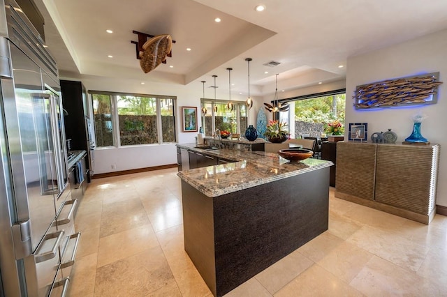 kitchen with a large island, a tray ceiling, high quality fridge, hanging light fixtures, and light stone countertops