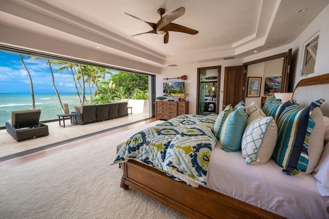 bedroom with a water view, ceiling fan, a tray ceiling, and hardwood / wood-style floors