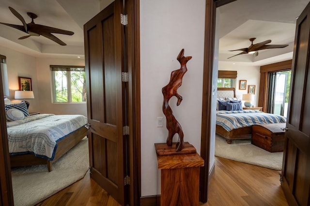 bedroom featuring ceiling fan, a tray ceiling, and light hardwood / wood-style flooring