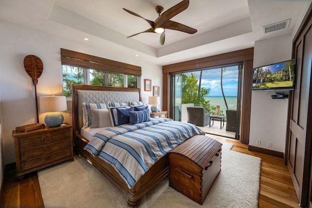 bedroom with ceiling fan, a tray ceiling, and light hardwood / wood-style flooring