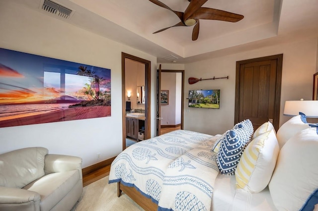 bedroom featuring ceiling fan, ensuite bathroom, a tray ceiling, and light hardwood / wood-style flooring