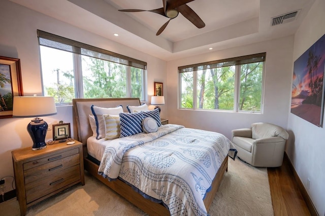 bedroom with ceiling fan, hardwood / wood-style floors, and a tray ceiling