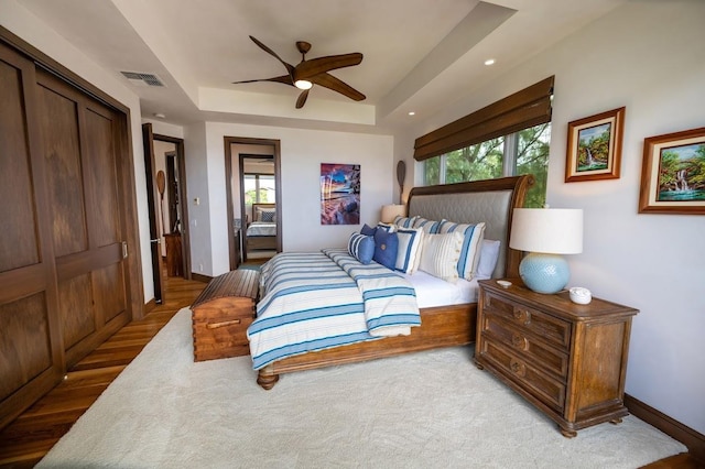 bedroom featuring ceiling fan, a closet, light wood-type flooring, and a raised ceiling