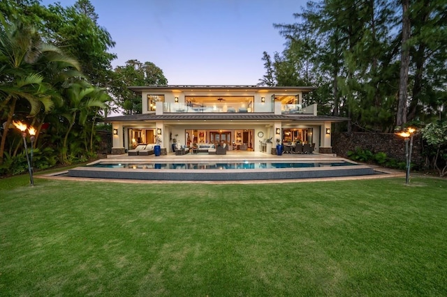 back house at dusk with a yard, an outdoor living space, and a patio