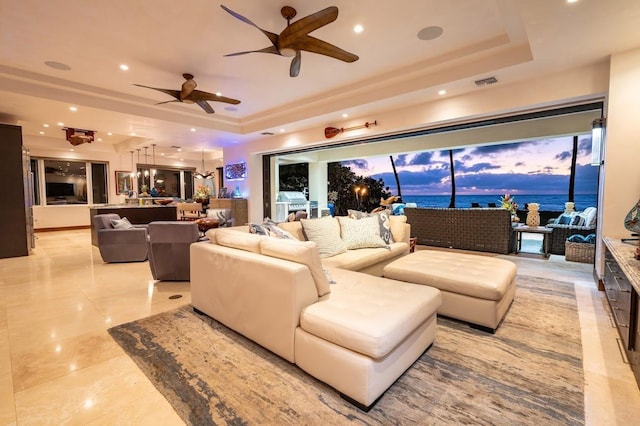 tiled living room with ceiling fan, a water view, and a raised ceiling