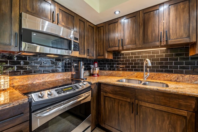 kitchen featuring sink, appliances with stainless steel finishes, backsplash, light stone counters, and dark brown cabinetry