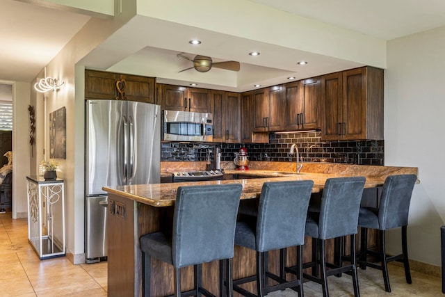 kitchen featuring light tile patterned flooring, a breakfast bar area, kitchen peninsula, stainless steel appliances, and backsplash