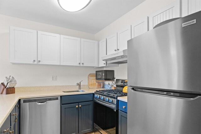 kitchen with blue cabinetry, appliances with stainless steel finishes, white cabinetry, and sink