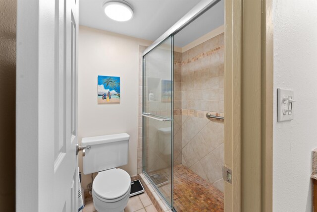 bathroom with tile patterned flooring, toilet, and a shower with shower door