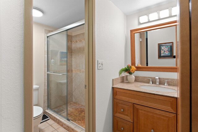 bathroom featuring tile patterned flooring, vanity, toilet, and a shower with shower door