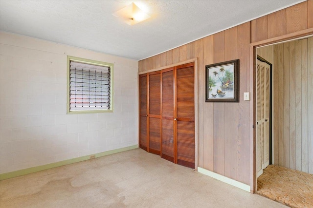 unfurnished bedroom with wooden walls, light colored carpet, and a textured ceiling