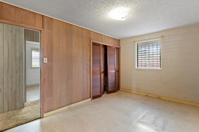 unfurnished bedroom with light colored carpet, wood walls, a textured ceiling, and a closet