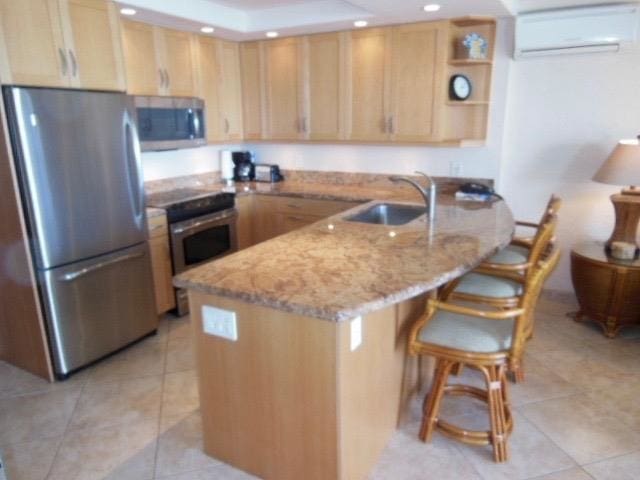 kitchen featuring light stone counters, sink, appliances with stainless steel finishes, light brown cabinetry, and a wall unit AC