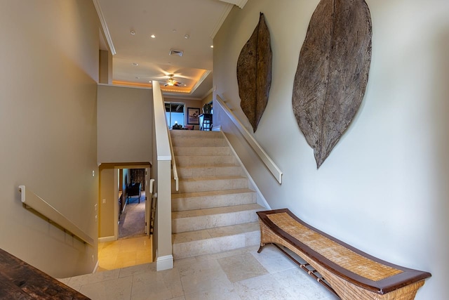 staircase with a tray ceiling, ceiling fan, and crown molding