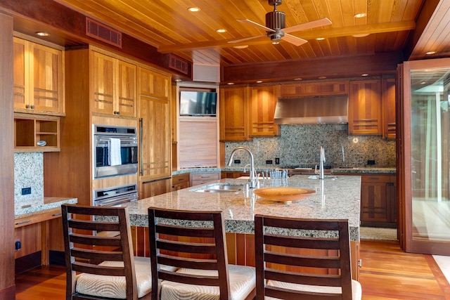 kitchen with sink, tasteful backsplash, light stone counters, light hardwood / wood-style floors, and wood ceiling