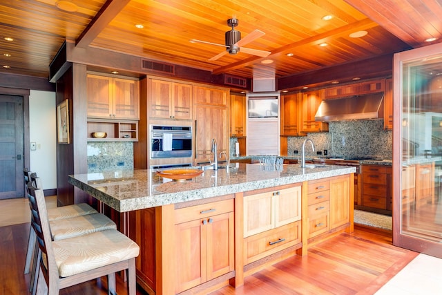 kitchen with light hardwood / wood-style flooring, ceiling fan, range hood, tasteful backsplash, and a kitchen bar