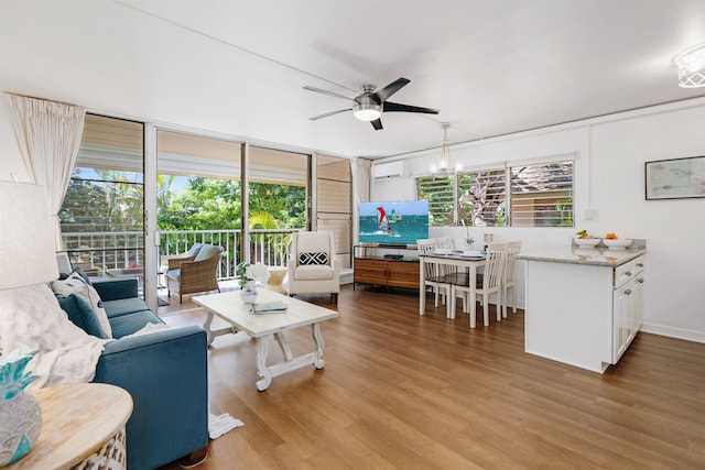 living room featuring a wall mounted air conditioner, wood-type flooring, and ceiling fan with notable chandelier