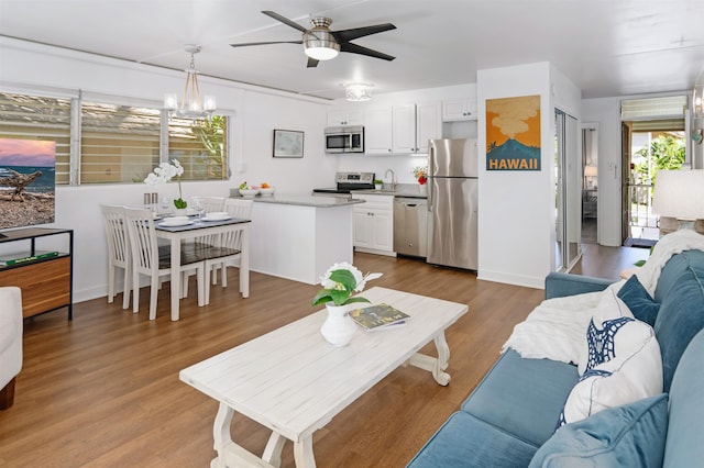 living room featuring light hardwood / wood-style flooring, ceiling fan with notable chandelier, and sink