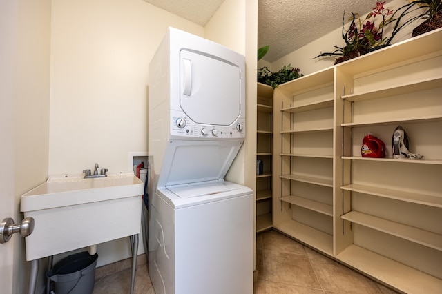 clothes washing area featuring sink, stacked washer / dryer, a textured ceiling, and light tile patterned floors