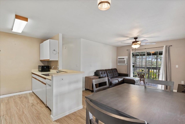 kitchen featuring sink, a wall mounted AC, white cabinets, kitchen peninsula, and light wood-type flooring