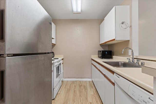kitchen with white appliances, a sink, white cabinetry, light countertops, and light wood finished floors