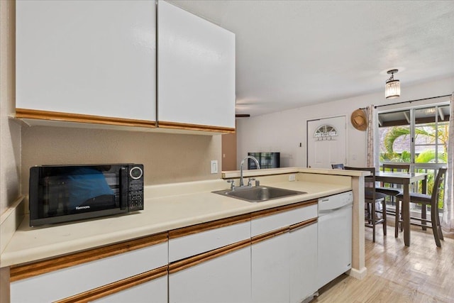 kitchen with black microwave, white dishwasher, light countertops, white cabinetry, and a sink
