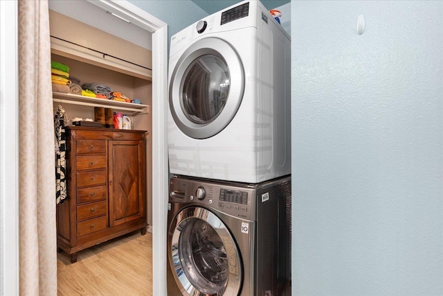 clothes washing area with light wood-type flooring, laundry area, stacked washer / drying machine, and a textured wall