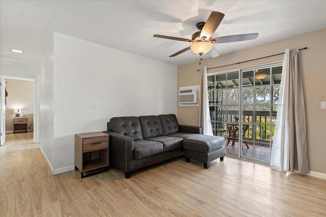 living room featuring a wall unit AC, light wood-style flooring, baseboards, and ceiling fan