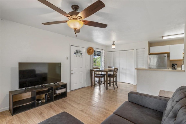 living area with light wood-type flooring, a ceiling fan, and baseboards