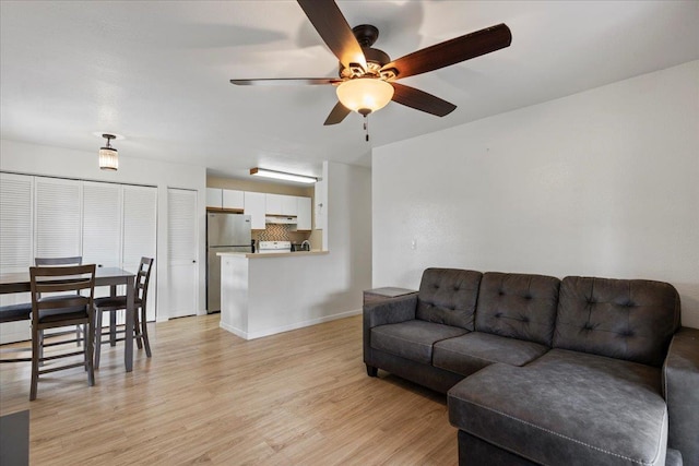 living area featuring light wood-style floors, ceiling fan, and baseboards
