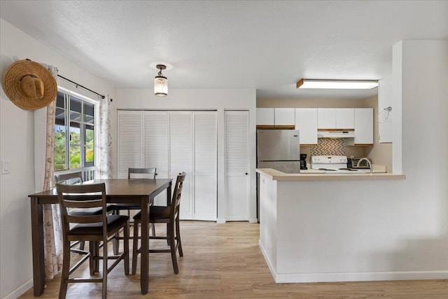 dining area featuring light wood-style floors, a textured ceiling, and baseboards