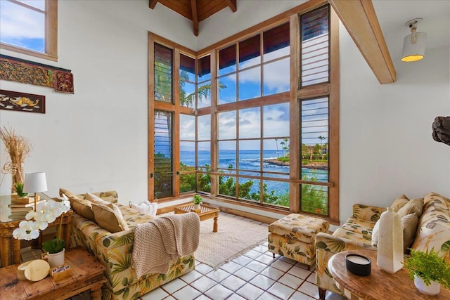 sitting room featuring a towering ceiling, a healthy amount of sunlight, a water view, and beam ceiling