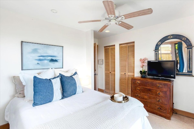 bedroom featuring light carpet, two closets, and ceiling fan