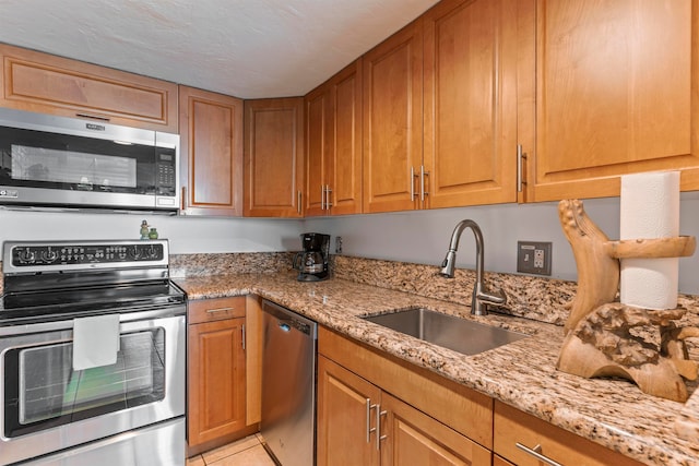 kitchen featuring light tile patterned floors, light stone counters, stainless steel appliances, sink, and a textured ceiling